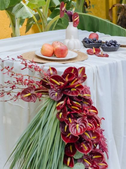Introducing our Orchard Table, an ode to intimate celebrations. A dramatic cascade of red anthuriums and tropical leaves flows from the table, set with fresh apples and grapes.
