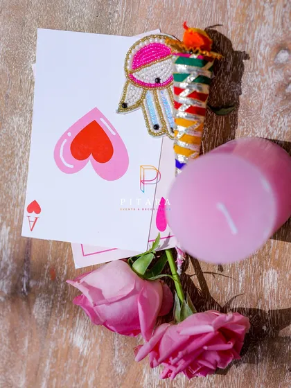 A flat lay of some of the custom stationery and favors, including a playful playing card and a beaded brooch, all tied into the event's color scheme and theme.