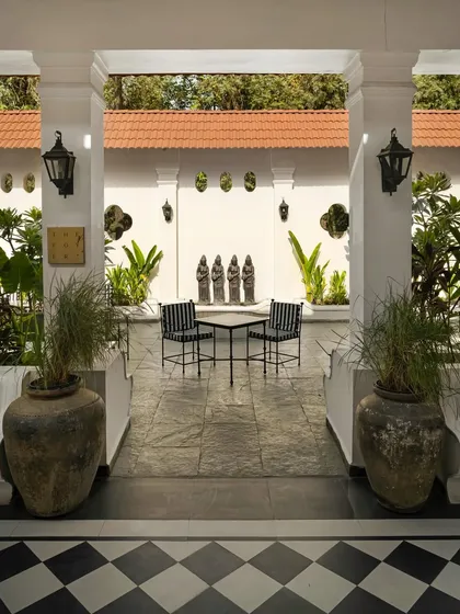 The outdoor foyer, where the interior's checkerboard floor extends to meet a tranquil courtyard. The space is framed by white columns, creating a seamless transition between inside and out.