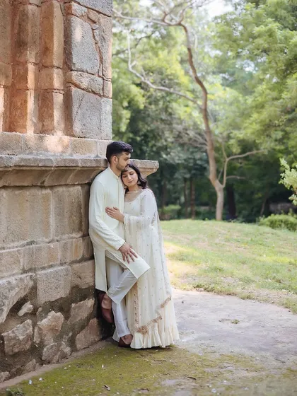A full-length portrait of a couple leaning against an ancient stone wall, a quiet and romantic pose.