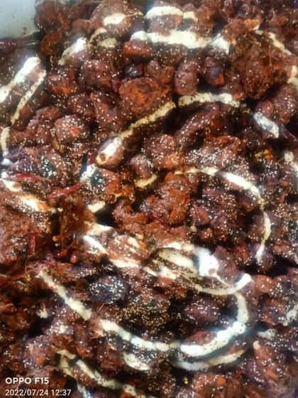 A rich, dark chicken dish, possibly a chili chicken or a similar dry starter, drizzled with mayonnaise and sesame seeds.