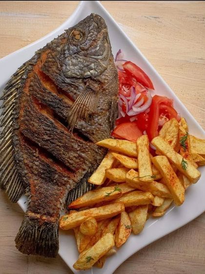 A whole fried fish served with a side of crispy french fries and a fresh salad. A simple, classic, and satisfying main course option for your event menu.