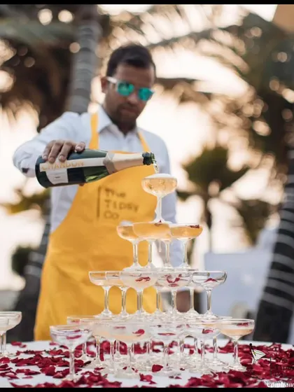 Our founder, Sid, looking cool and focused while pouring a champagne tower at a beach event. The yellow apron adds a pop of our brand's color to the scene.