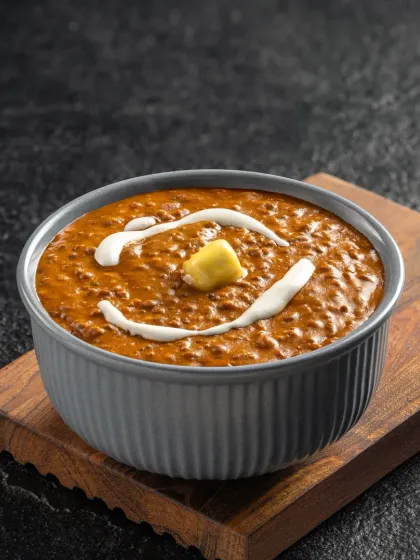 A classic Dal Makhani, with a swirl of cream and a dollop of butter. The dark, moody lighting enhances the rich, creamy texture of this beloved dish.