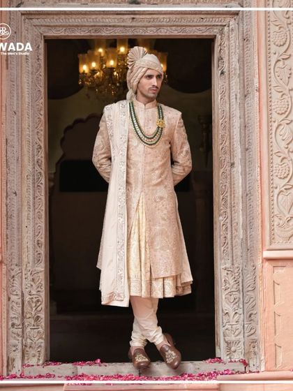 A full-length shot of the groom, showcasing the flow and structure of the sherwani. The layered style and the elegant drape of the stole add to the majestic feel.