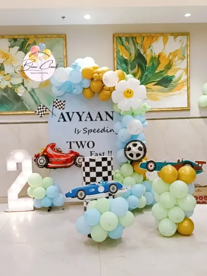 A creative "speeding two fast" race car theme for a second birthday. This decoration features a custom backdrop, balloon arrangements in theme colors, car cutouts, and a large marquee number '2'.