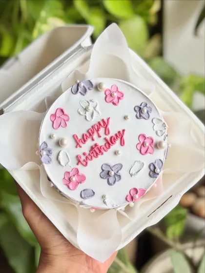 Delicate florals, soft pastels, and a whole lot of charm. This "Happy Birthday" bento cake features tiny flowers in pink, purple, and white, dotted with pearls.