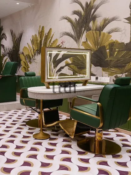 A close-up of the styling station at Looks Salon, where the custom-designed mirror with integrated lighting sits atop a fluted white counter. The rich green leather and brushed gold accents of the chair add a layer of opulence.