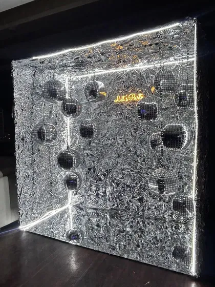 A unique 3D photo op. This silver shimmer cube is lit with neon strips and filled with disco balls, creating a futuristic and immersive space for guests to take pictures.
