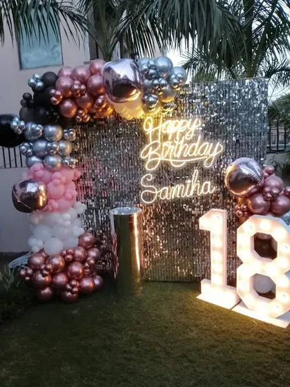 An outdoor 18th birthday party setup on the grass, with a sequin wall, personalized neon sign, and marquee numbers.