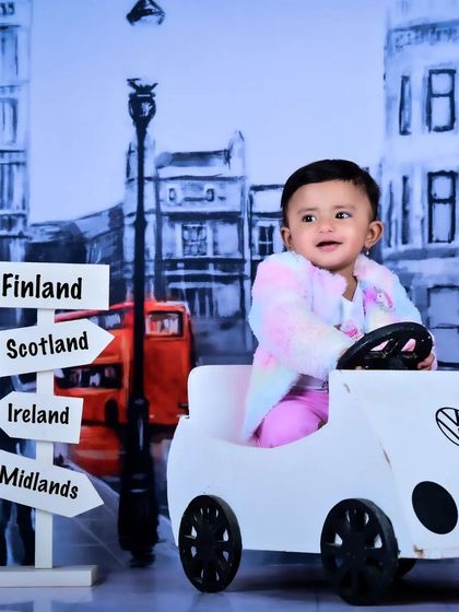 A little traveler in a toy car against a backdrop of London, with a signpost pointing to different destinations.