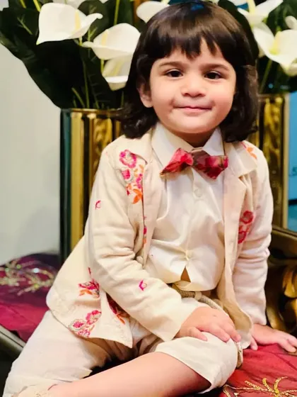 A young model in a formal kids' wear ensemble. This custom look features an off-white suit with a beautifully embroidered floral blazer and a matching bow tie.