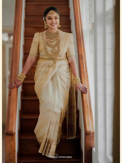 The bride descending a staircase, her traditional gold and cream saree looking absolutely regal.