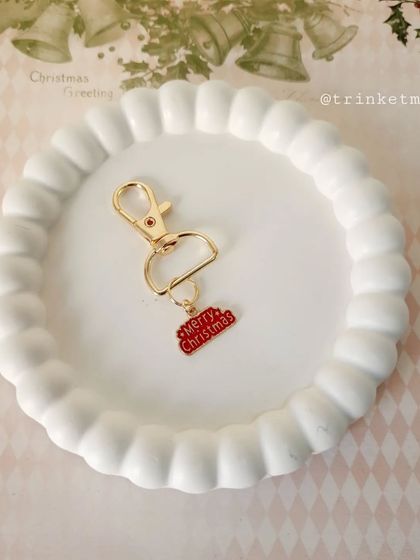 A 'Merry Christmas' word charm keychain, perfect for spreading holiday cheer. The bright red enamel makes it stand out.
