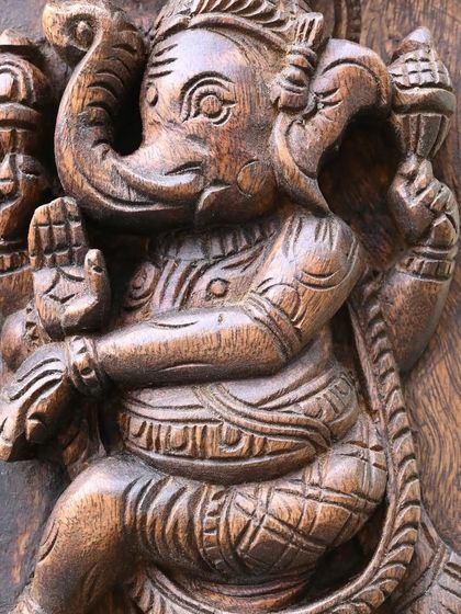 A close-up of a Ganesha form in a dynamic pose from the Ashta Ganesha panel, showcasing the energy captured in the wood.