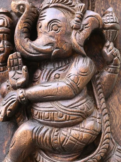 This close-up highlights the dynamic posture of a dancing Ganesha from the Ashta Ganesha panel. The sense of movement and joy is skillfully rendered in the solid wood.