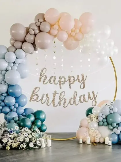 A beautiful and delicate birthday balloon hoop. The gradient of colors from teal to blush pink, combined with fresh flowers and a glittery banner, creates a soft and artistic look.