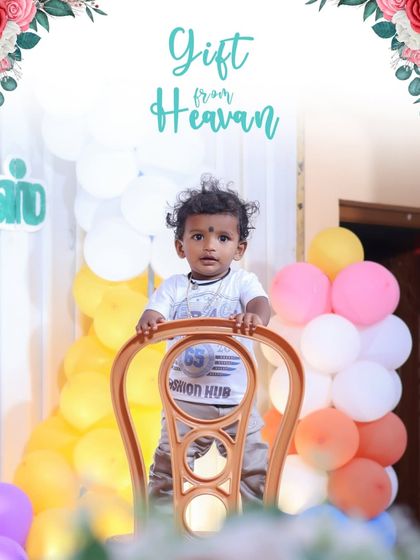 A "Gift from Heaven" indeed. This photo shows the birthday boy standing tall with the help of a chair, surrounded by a beautiful arch of balloons, perfectly capturing his curious nature.
