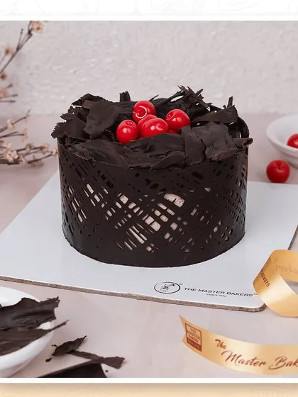A close-up of our classic Black Forest cake, showing the intricate chocolate cage, rich chocolate shavings, and bright red cherries that make this dessert a timeless favorite.