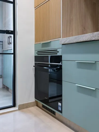 The built-in oven is seamlessly integrated into the mint green and wood cabinetry. This thoughtful placement ensures the kitchen remains functional and visually cohesive, with a smooth transition between different materials and appliances.