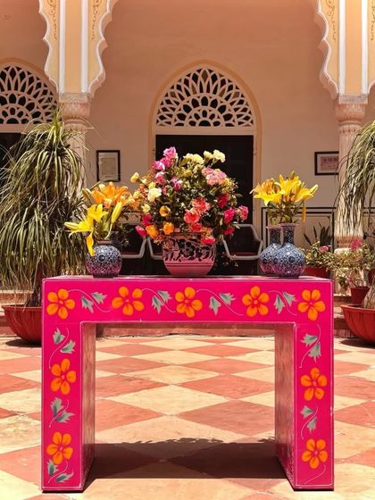 A hand-painted pink table with a floral centerpiece. This unique piece of furniture adds a pop of color and artistic flair to the traditional decor.