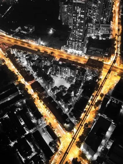 A creative black-and-white aerial shot of Mumbai at night, with the golden light trails of traffic forming a "V" shape, like veins of the city.
