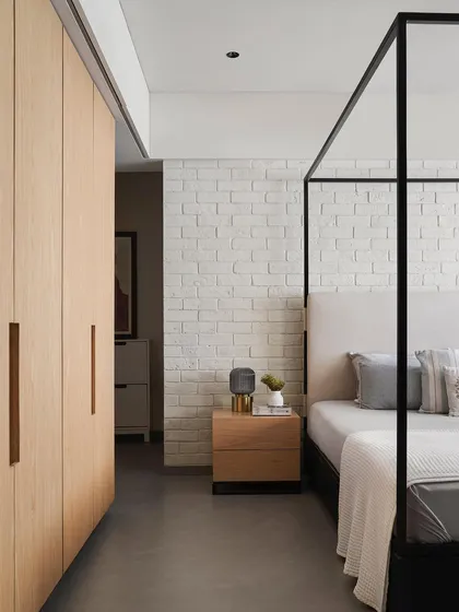 This bedroom features a sleek, black metal four-poster bed I designed, set against a textured white brick wall. The custom ash wood side table and handle-less wardrobes continue the theme of clean lines and contrasting materials.