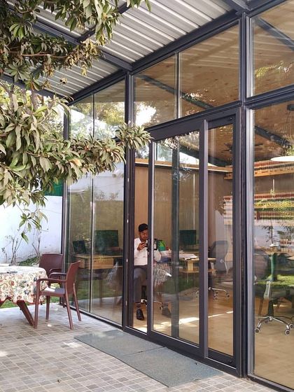 The Gazebo 1.0 office space seen from the outside patio. The full-height glass walls dissolve the boundary between the workspace and the garden, allowing the employees to feel connected to the outdoors throughout the day.