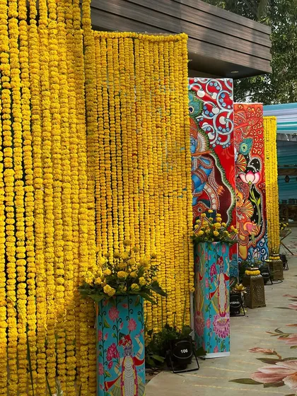 A decor detail showing a wall of yellow marigolds next to pillars decorated with colorful, traditional Indian paintings.