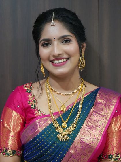 A close-up of a Varapooje look. The makeup is clean and traditional, with a bright pink lip that beautifully contrasts with her deep blue and pink Kanjeevaram saree.