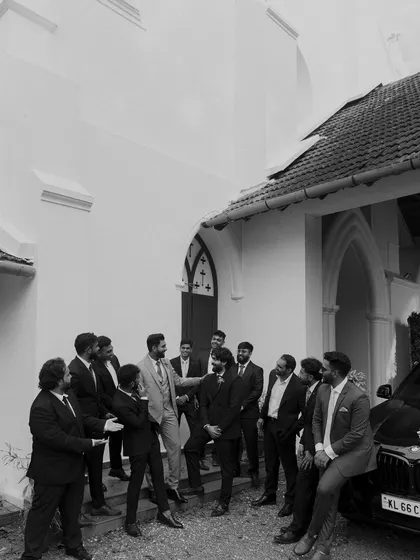 The groom shares a laugh with his groomsmen outside the church. This candid black and white shot captures the relaxed and happy atmosphere among friends before the ceremony.