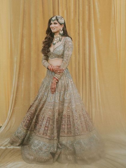 A full-length portrait against a simple backdrop, allowing the bride's detailed lehenga and flawless makeup to be the main focus.