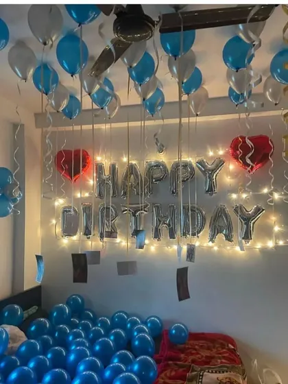 A simple birthday room surprise with blue balloons on the floor, "Happy Birthday" foil letters, and fairy lights.