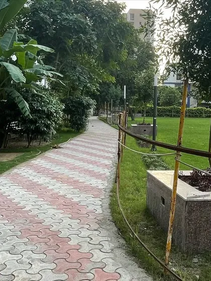 The paved path runs alongside the main lawn, with trees in stone planters placed at regular intervals. This design element adds rhythm and structure to the large open space.