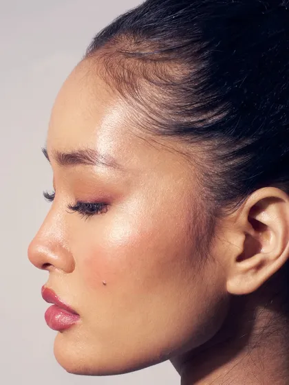 A profile shot highlighting the "glass skin" effect. The highlighter catches the light beautifully, and the soft pink tones on the eyes and lips complete the look.