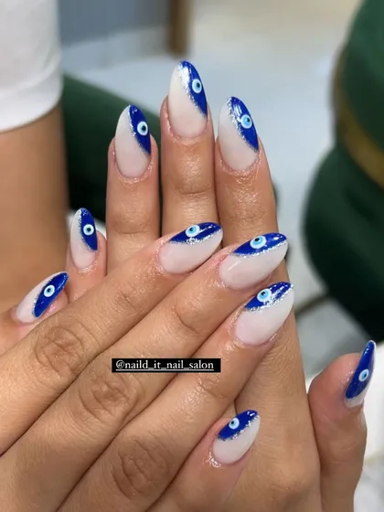 A trendy and protective evil eye design. We combine a modern French manicure style with hand-painted evil eye motifs on almond-shaped extensions, adding a touch of sparkle with fine blue glitter for a unique and stylish look.