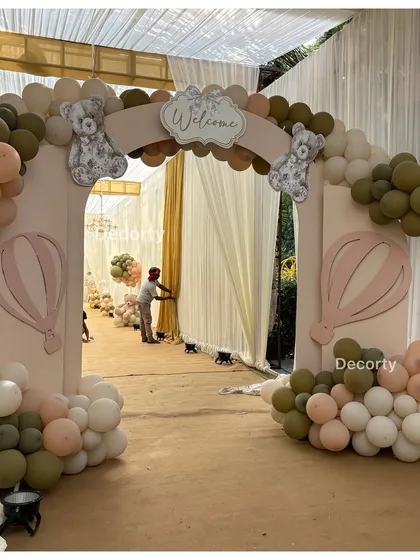 An entrance arch for a neutral-toned teddy bear theme, using olive green, beige, and pink balloons with hot air balloon cutouts.