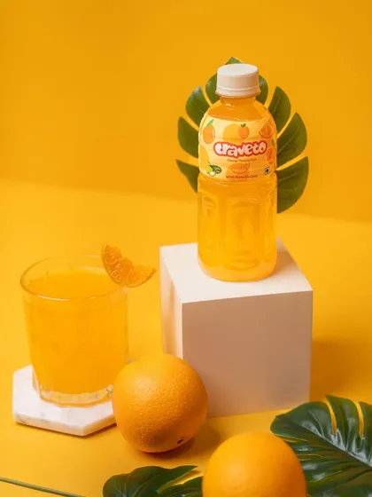 A styled shot of an orange drink with a glass, fresh oranges, and props on a bright yellow background. This setup creates a complete scene, perfect for a website banner or advertisement.