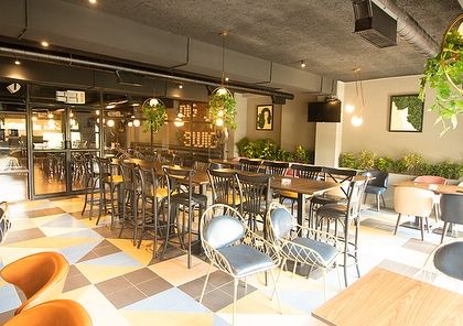 The main dining area at Dank, where hanging planters and potted plants are used to soften the industrial-chic interior. The greenery adds a touch of life and color to the space.