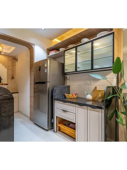 A dedicated section for the refrigerator and additional storage, featuring glass-fronted overhead cabinets to display crockery.