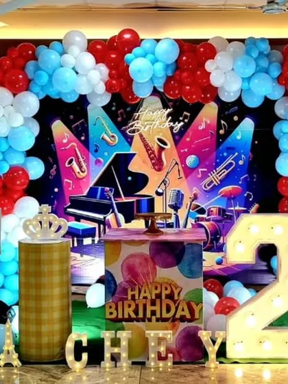 A vibrant music-themed birthday party for a 2-year-old, with a colorful backdrop of musical instruments and a red, white, and blue balloon arch.