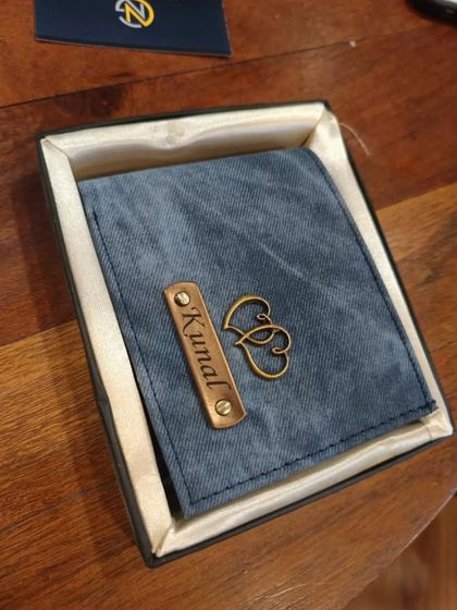 A personalized blue denim wallet for 'Kunal' with a double heart charm, presented in its gift box.