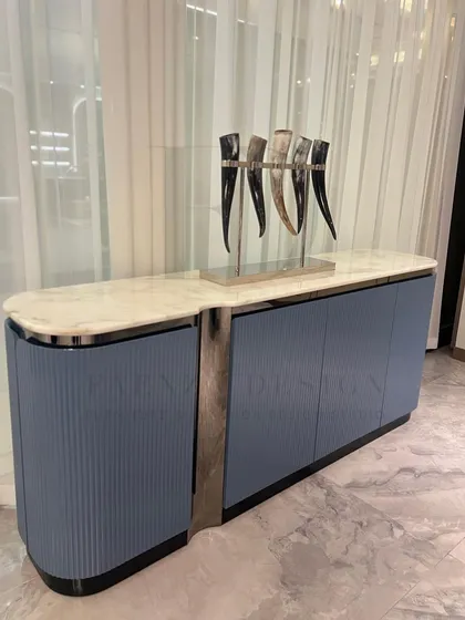 This elegant sideboard features a white marble top and a body finished in a dusty blue Duco paint. The fluted, curved doors and chrome accents give it a sophisticated, Art Deco feel.