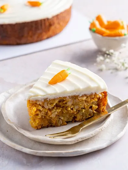 A perfect slice of our Old Fashioned Carrot Cake, revealing a moist, spice-flecked interior packed with carrots and nuts. Topped with a generous layer of smooth cream cheese frosting, it's comfort in its most delicious form.