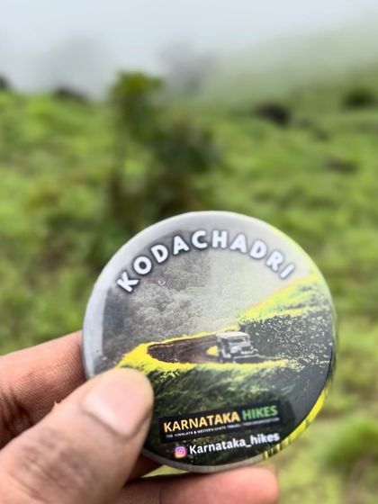 Our Kodachadri badge held against the misty green hills, a perfect souvenir.