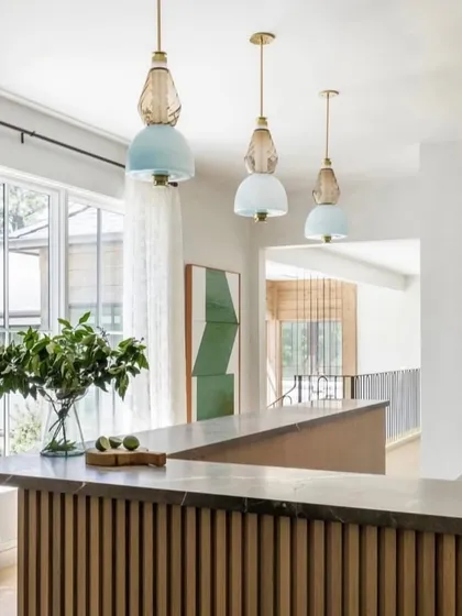 A trio of Luna Kaleido pendants in soft blue and amber tones, hung at varying heights over a kitchen bar. This creates a playful yet elegant composition.