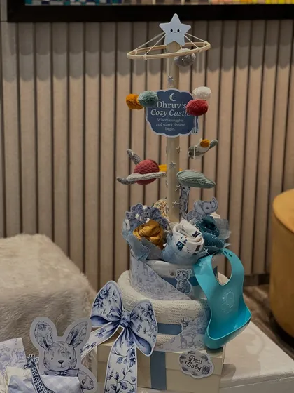 This is 'Dhruv's Cozy Castle', a multi-tiered diaper cake I designed. It's topped with a handmade mobile featuring planets and stars, and includes a practical silicone bib.