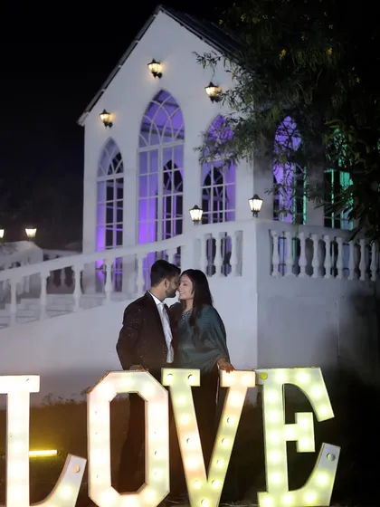 A romantic pre-wedding photo in front of our lit-up chapel at night, with the 'LOVE' prop adding to the magical atmosphere.