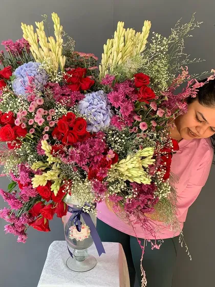 Go big and go beautiful. Here I am with one of my massive, custom vase arrangements, overflowing with a vibrant mix of red roses, blue hydrangeas, and fragrant Rajnigandha. This is the kind of lush, colorful energy I love to bring to any space or celebration.