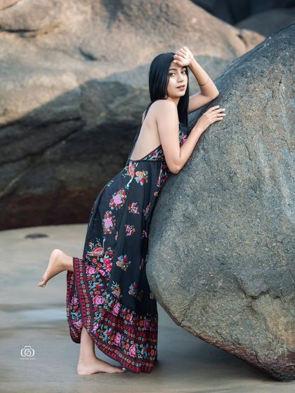 A full-length shot of the model in a floral dress, leaning against a large rock. The pose is casual and elegant, perfect for a fashion lookbook.